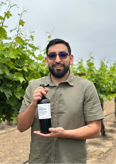 David Salazar seated on the tailgate of his truck in the vineyard, glass of wine in hand